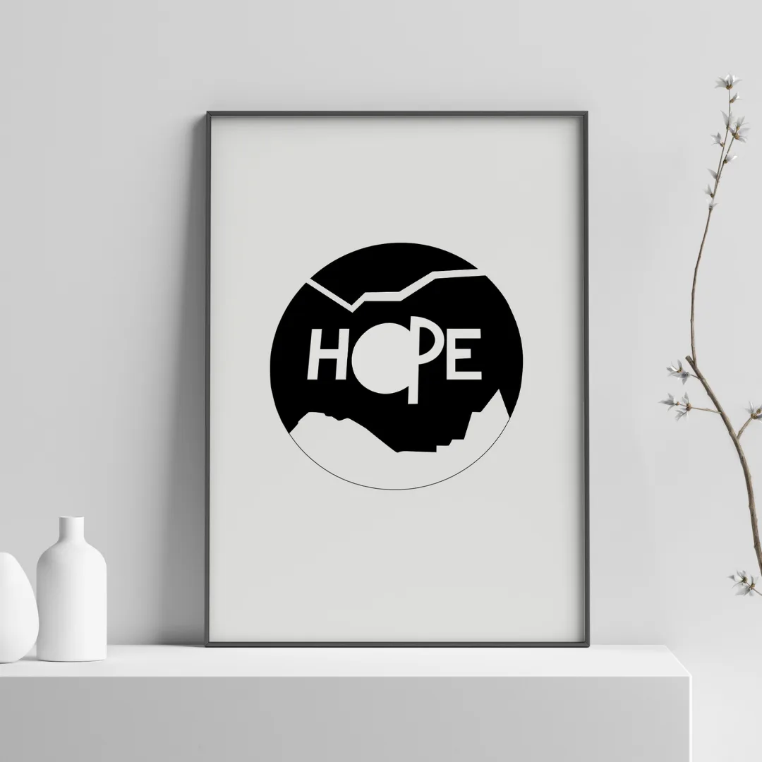 A framed black-and-white poster reading "HOPE" set inside a circle of mountains, styled as wall art on a shelf with vases and a branch